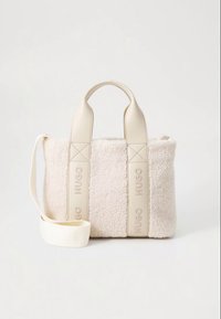 Geantă bej din imitație de blană de oaie, cu mânere din piele crem și curea detașabilă. Prezintă o formă ușor structurată și sigla „HUGO” în relief.