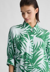 Camicia button-up verde e azzurro chiaro con motivo foglia di palma, realizzata in un tessuto morbido, con colletto e maniche arrotolate.