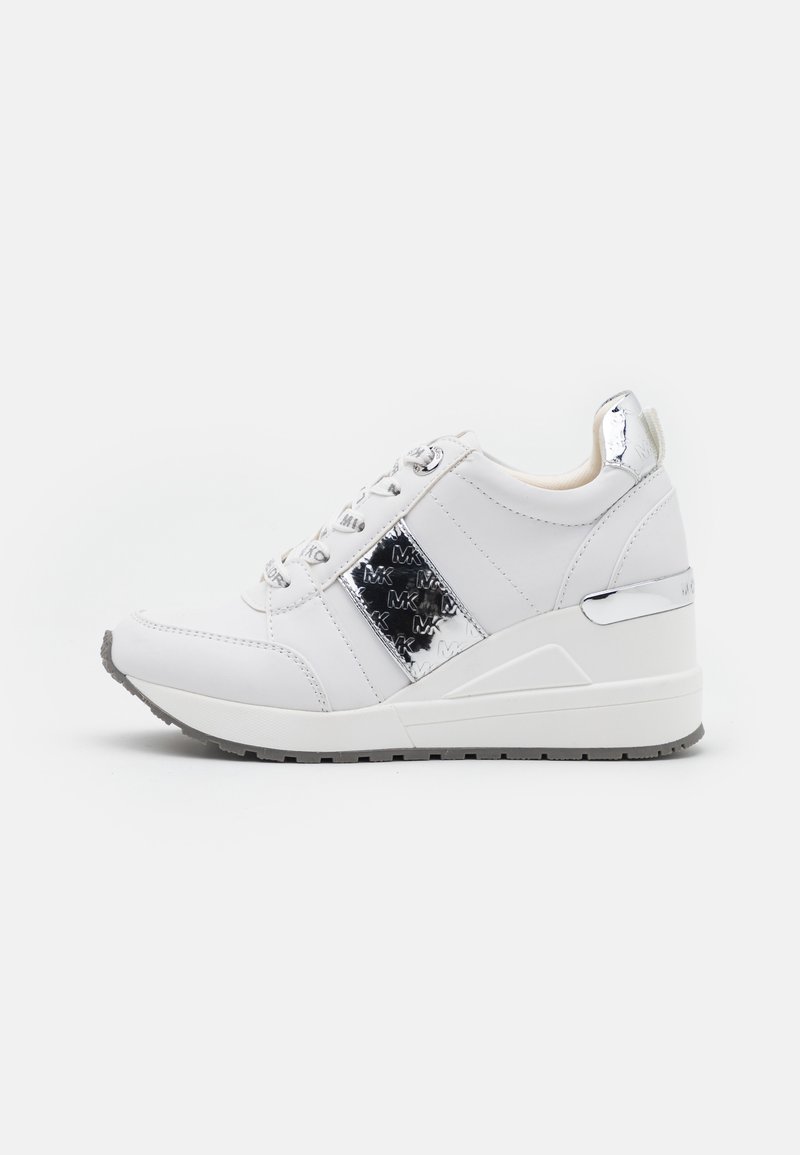 Zapatillas deportivas blancas con cuña y acentos metálicos plateados, detalle del logo "MK" en el lateral, cordones blancos y suela texturizada gris.