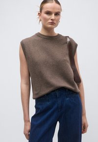 Καφέ αμάνικη πλεκτή μπλούζα με ριμπ στρογγυλή λαιμόκοψη, συνδυασμένη με ψηλόμεσα σκουρό μπλε τζιν, με πίσω τσέπες και λεία υφή.