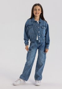 Denim jakna z gumbom spredaj in dvema žepoma na prsih; v kombinaciji z ohlapnimi cargo hlačami z stranskimi žepi. Svetlo pranje z elastičnimi manšetami.