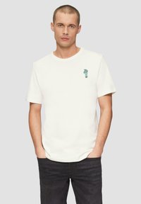 Witte katoenen t-shirt met korte mouwen, voorzien van een klein blauw grafisch ontwerp op de linkerborst. Gedirigeerd met een donkere spijkerbroek.