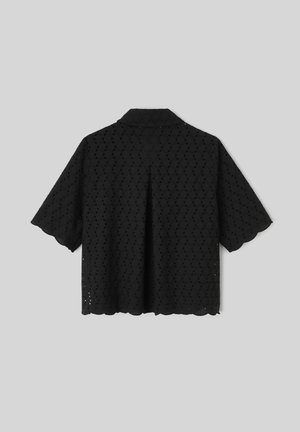 Blouse noire à manches courtes avec motif ajouré, bords festonnés et pli au dos, présentée sur un fond gris clair.