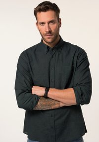 Camisa abotonada verde oscuro con una textura a rayas y un sutil patrón de hojas, con mangas largas y un cuello normal.