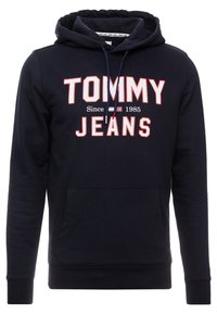 Námořnická modrá mikina s kapucí a přední kapsou, s nastavitelnou šňůrkou a logem "TOMMY JEANS Since 1985" v bílé a červené barvě.