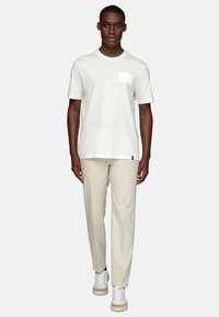 White cotton t-shirt with a chest pocket, paired with beige trousers and white sneakers featuring a tan sole. Simple, clean design.