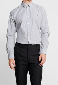 Camicia a righe in blu navy e bianco, realizzata in cotone, con colletto classico e maniche lunghe, abbinata a pantaloni scuri.
