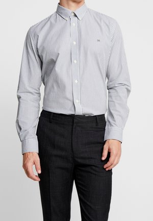 Camisa de botones a rayas en azul marino y blanco, confeccionada en algodón, con un cuello clásico y mangas largas, combinada con pantalones oscuros.