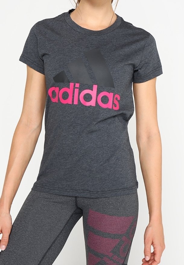 Kobieta w ciemnoszarej koszulce Adidas z różowym logo oraz dopasowanych legginsach z różowymi geometrycznymi wzorami.