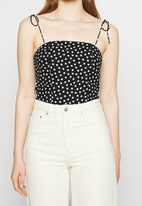 Top nero con stampa floreale bianca, spalline sottili e dettagli con lacci regolabili. Indossato con jeans in denim bianco a vita alta.