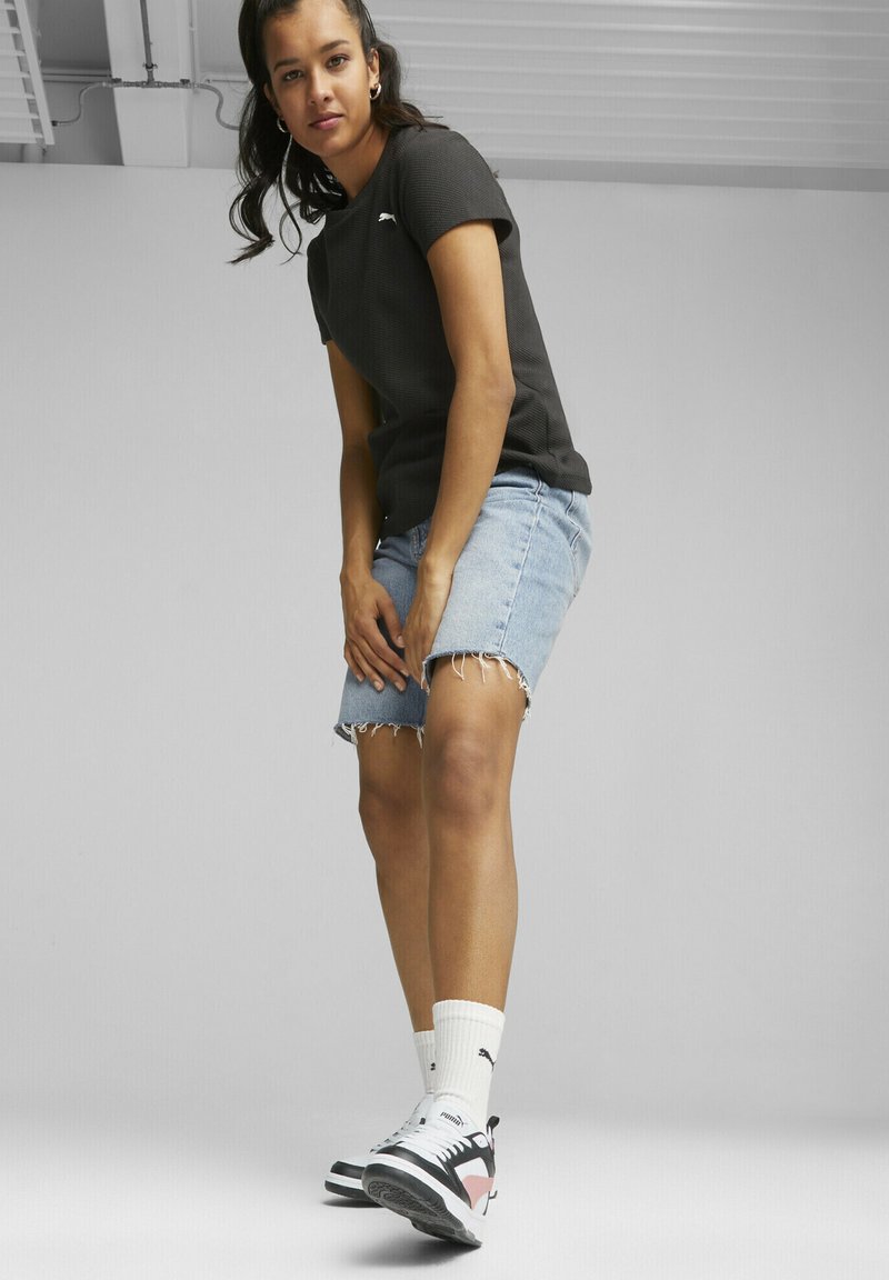 T-shirt noir à côtes, short en denim avec ourlet effiloché, baskets noir et blanc avec accent rose, et chaussettes blanches avec logo.