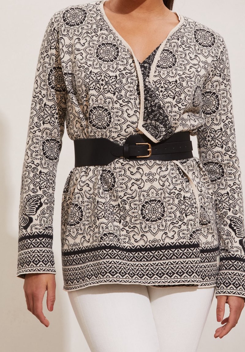 Svart och krämfärgad mönstrad kofta med en omslagdesign, kontrasterande kanter och ett svart bälte. Långa ärmar och intrikata motiv genom hela plagget.