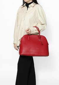 Rode leren handtas met een gestructureerde vorm, twee bovenhandvatten en een ritssluiting. Het oppervlak is getextureerd en heeft subtiele stikdetails.