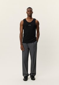 Μαύρο αμάνικο τοπ με ραβδωτή υφή, με λευκό λογότυπο· συνδυασμένο με γκρι, φαρδιά παντελόνια και μαύρα παπούτσια.