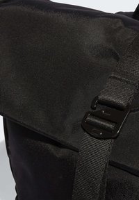 Närbild av en svart tygväska med en texturerad klaff och justerbar rem som hålls på plats av ett svart metallspänne.