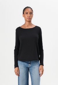 Black long-sleeve top made of cotton with a round neckline and a relaxed fit, paired with light blue jeans. Notable seams and minimal branding.