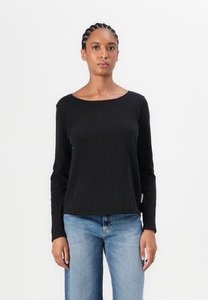 Black long-sleeve top made of cotton with a round neckline and a relaxed fit, paired with light blue jeans. Notable seams and minimal branding.