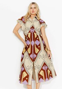 Robe en button-up de couleur taupe avec de grands motifs géométriques en brun, lavande et jaune. Manches courtes et poches latérales sont très présentes.