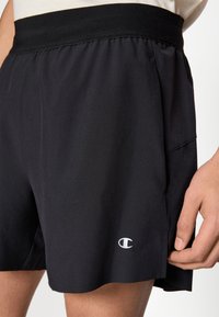 Μαύρο αθλητικό σορτς με ελαστική μέση, που διαθέτει ένα μικρό λογότυπο στο κάτω αριστερό μέρος και ελαφριά, λεία υφή.