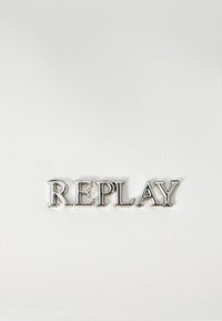 Lettres métalliques argentées épelant "REPLAY" sur un fond blanc texturé et lisse, centrées dans l'image.