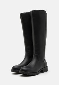 Bottes noires montantes en cuir lisse. Bout arrondi et talon empilé. Coutures détaillées sur les bords supérieurs. Semelle extérieure en caoutchouc.