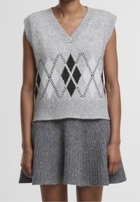 Personne portant un gilet sans manches en tricot gris avec un motif diamant noir et blanc, et une jupe en tricot côtelé gris.