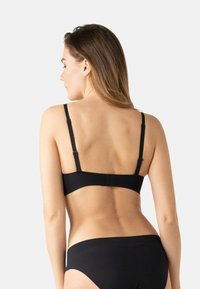 Soutien-gorge noir sans coutures avec bretelles ajustables, fermeture à crochets à l'arrière, texture douce et design minimaliste, complété par des sous-vêtements assortis.
