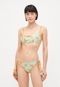 Bikini set z kvadratnim izrezom, mint zelena tkanina z oranžnimi cvetličnimi vzorci in detajli s vezanjem ob straneh na bikini spodnjem delu.