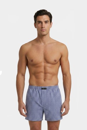 Shirtloser Mann steht, trägt blau-weiß karierte Boxershorts vor einem einfarbigen hellgrauen Hintergrund.