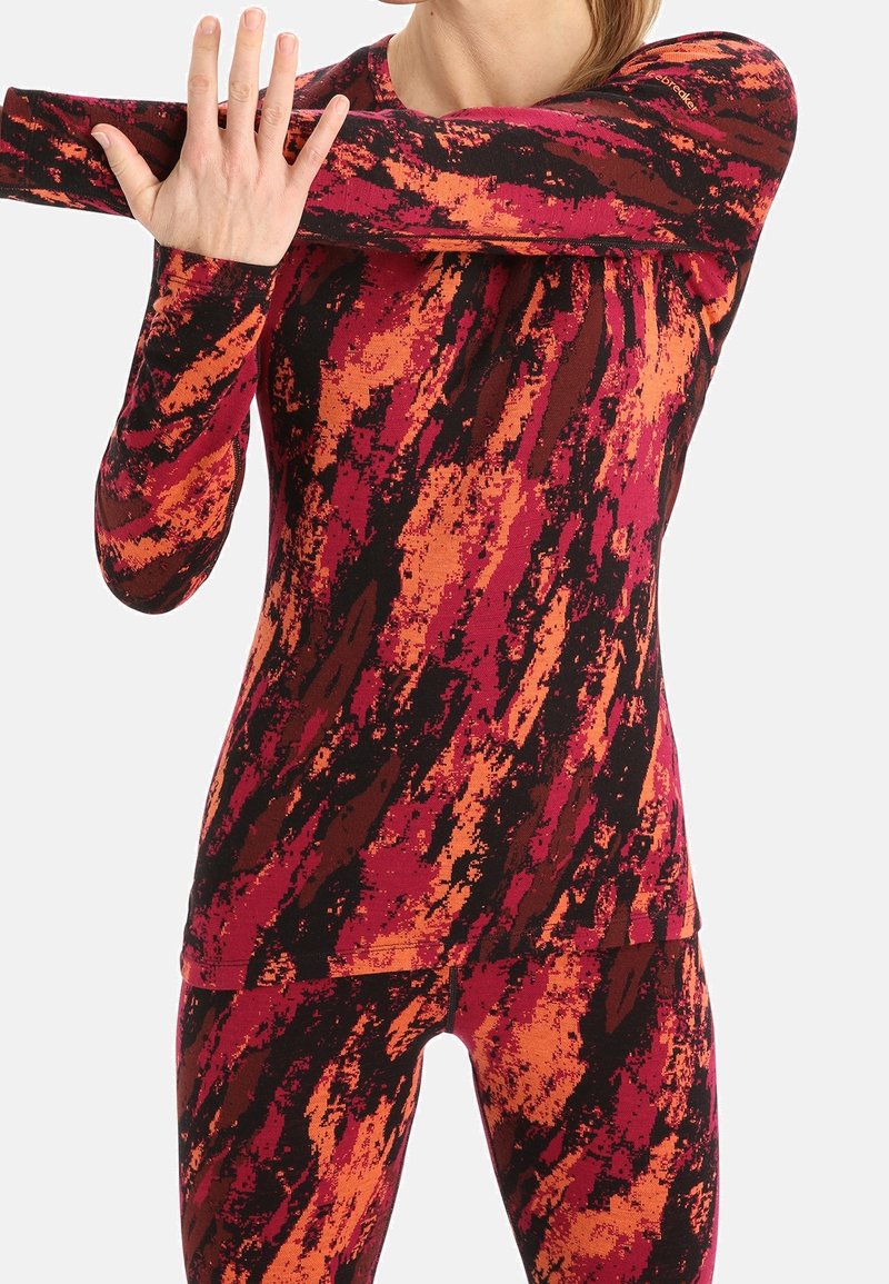 Pitkähihainen urheilupaita punaisen, mustan ja oranssin abstraktilla kuviolla, valmistettu joustavasta materiaalista, pyöreällä pääntiellä ja istuvalla mallilla.