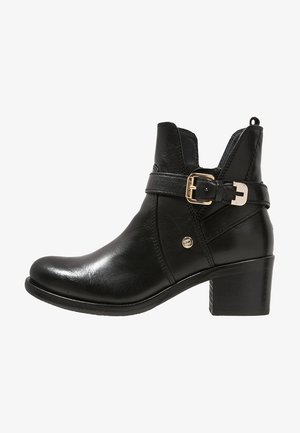 Bottine en cuir noir avec un talon empilé, une sangle à boucle sur le côté, une languette à l'arrière et un petit logo métallique.