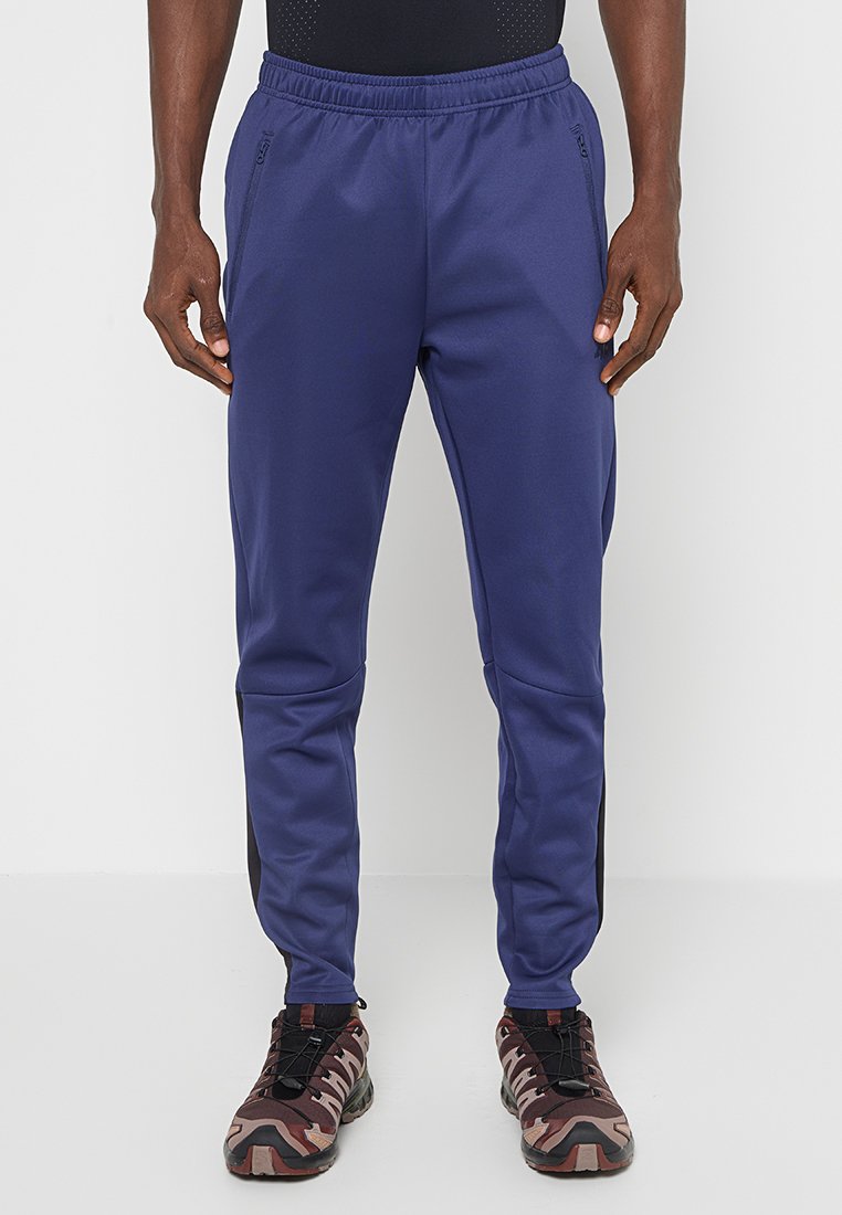 Granatowe spodnie sportowe z elastycznym paskiem, bocznymi kieszeniami oraz kontrastowymi czarnymi panelami po bokach, wykonane z gładkiego, lekkiego materiału.