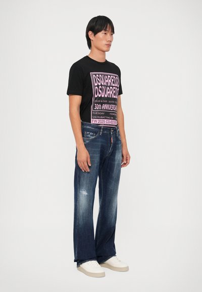 Camiseta negra con estampado gráfico rosa, combinada con jeans de mezclilla oscura desgastados y zapatillas blancas. Diseño sencillo, corte relajado.