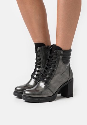 Botas tobilleras metálico gris con cordones negros y parte superior texturizada. Presentan un tacón rectangular y cremallera lateral; el cuello estriado acentúa el diseño.