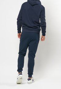 Marinblå sweatshirt och joggers i bomullsblandat tyg. Sweatshirten har huva; joggers har elastiska muddar och en slät textur.