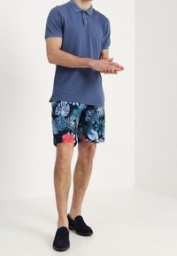 Polo skjorte i navy med krave, parret med navy blomster shorts, der har grønne blade og røde blomster. Sorte slip-on sko.