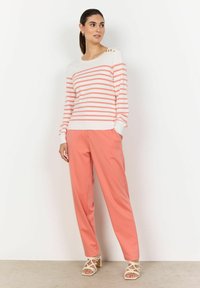 Suéter a rayas rojas y blancas con detalles en botones dorados en el hombro, combinado con pantalones jogger color coral y sandalias beiges con tiras.