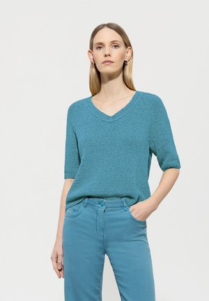 Türkises, gestricktes Kurzarmoberteil mit V-Ausschnitt, kombiniert mit passenden hellblauen Hosen. Strukturierter Stoff, lockere Passform.