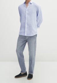 Lichtblauw linnen overhemd met knopen, relaxte pasvorm, lange mouwen. Een paar lichtblauwe denim jeans en donkere espadrilles met een geweven zool.