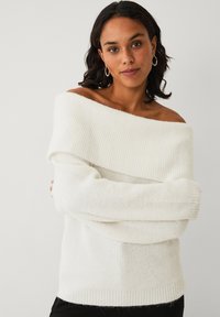 Off-the-shoulder hvid sweater lavet af et blødt, ribbet strikkemateriale med løse ærmer, der har en struktureret overflade og en afslappet pasform.