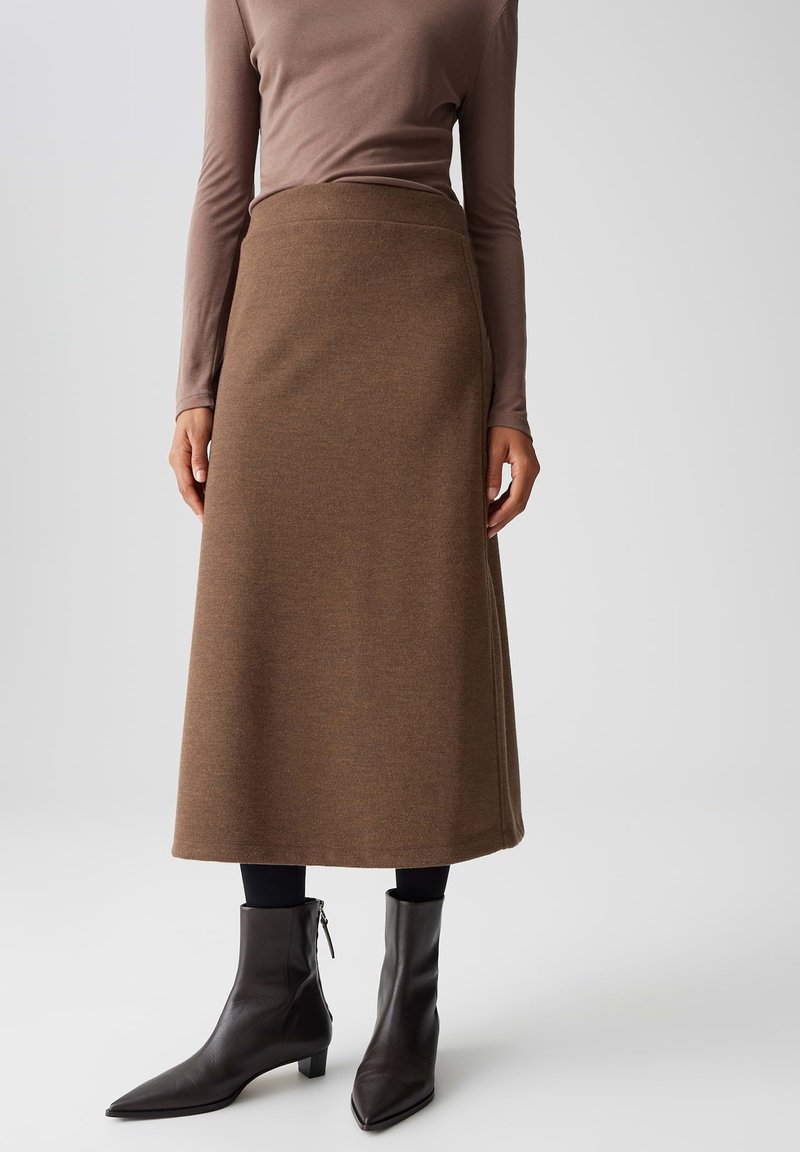 Gonna midi in maglia marrone con una texture liscia e vita alta, abbinata a stivali neri alla caviglia con punta appuntita e dettagli con zip.