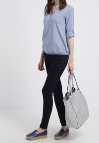 Blouse bleu clair à boutons ; jean foncé ; chaussures plates marines texturées ; grand sac à main gris doux avec doubles poignées.