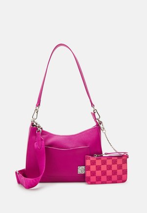 Leuchtend pinke Schultertasche mit passendem kleinem Täschchen, das an einer silbernen Kette befestigt ist, vor einem schlichten weißen Hintergrund.