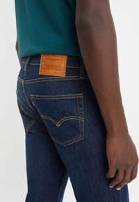 Mørkeblå denim jeans med oransje søm, merkevare lærlapp på midjebåndet og klassisk baklomme design.