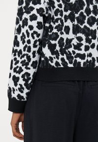 Sweter w czarno-białą panterę z teksturowanym wzorem. Rękawy i dół są czarne, co kontrastuje z wyrazistym wzorem.