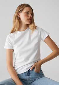 T-shirt bianco in cotone con maniche corte e scollatura rotonda, abbinato a jeans in denim blu. Texture liscia, design aderente e senza motivi visibili.