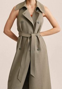 Gabardina caqui con diseño de doble botonadura, cuello grande y cinturón. Presenta botones redondos y una textura lisa.