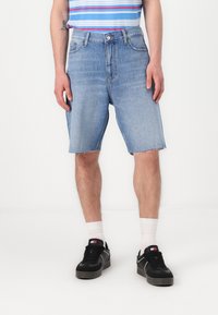 Lys blå denimshorts med rå kant, kombinert med sorte joggesko og hvite sokker. Skjorten har horisontale striper i blått og rødt.
