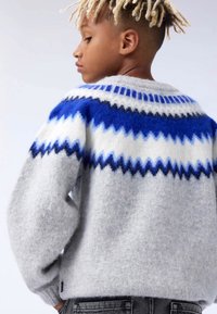 Siv sweater z teksturirano površino, s sinje-belimi cik-cak vzorci na yoku. Dolgi rokavi, okrogla izreza in sproščen kroj.
