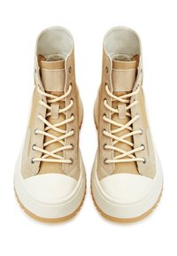 Pár béžových vysokých tenisek s bílými gumovými špičkami a silnými hnědými podrážkami, s krémovými tkaničkami a materiálem z semiše a textilu.